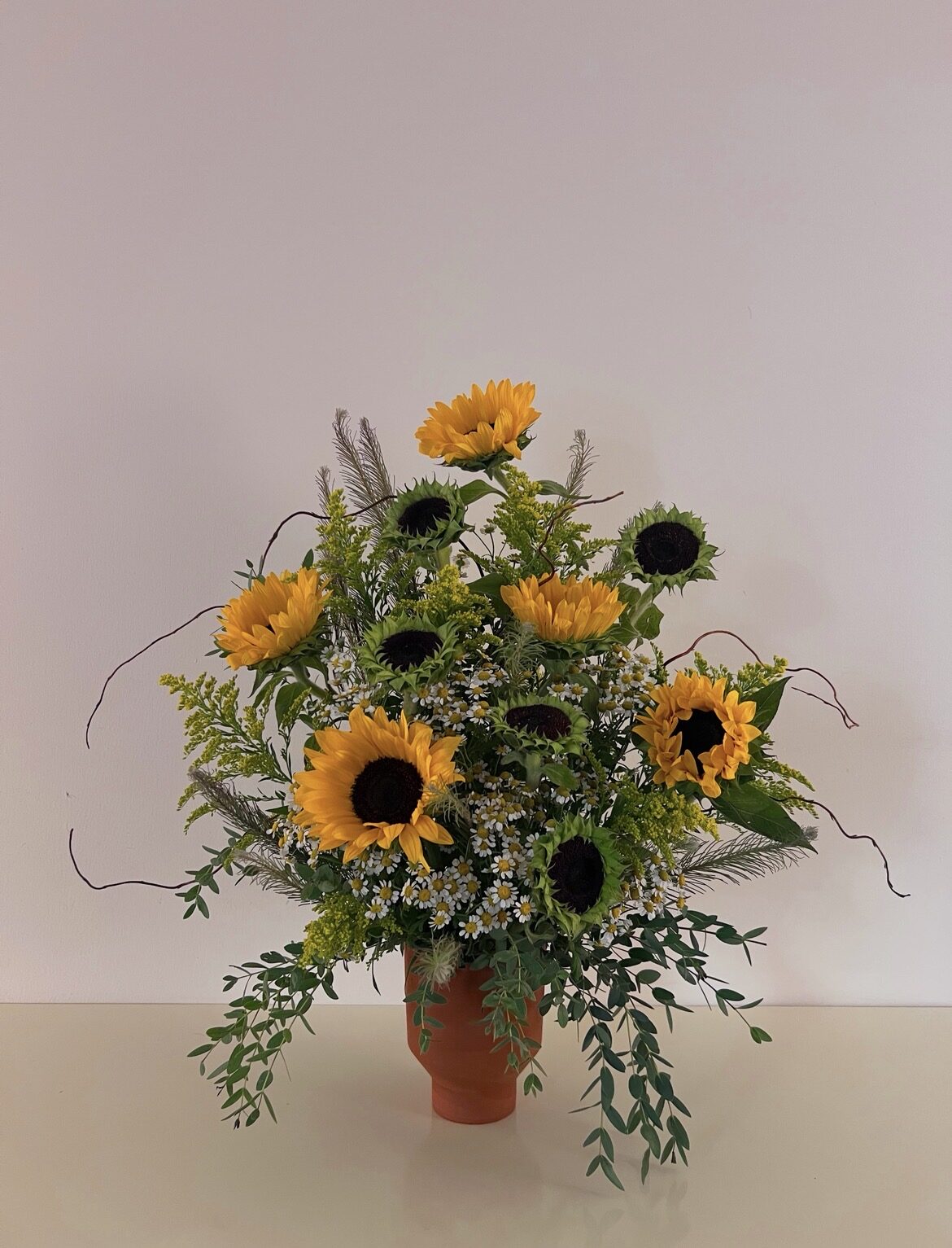 Sunflower arrangement with feverfew, goldenrod and curly willow in a terracotta vase